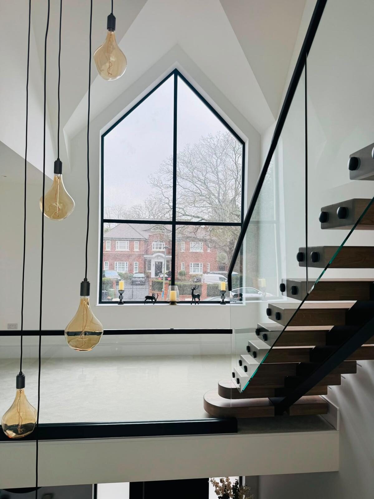 Full-height apex gable window in slim black aluminium above a floating staircase