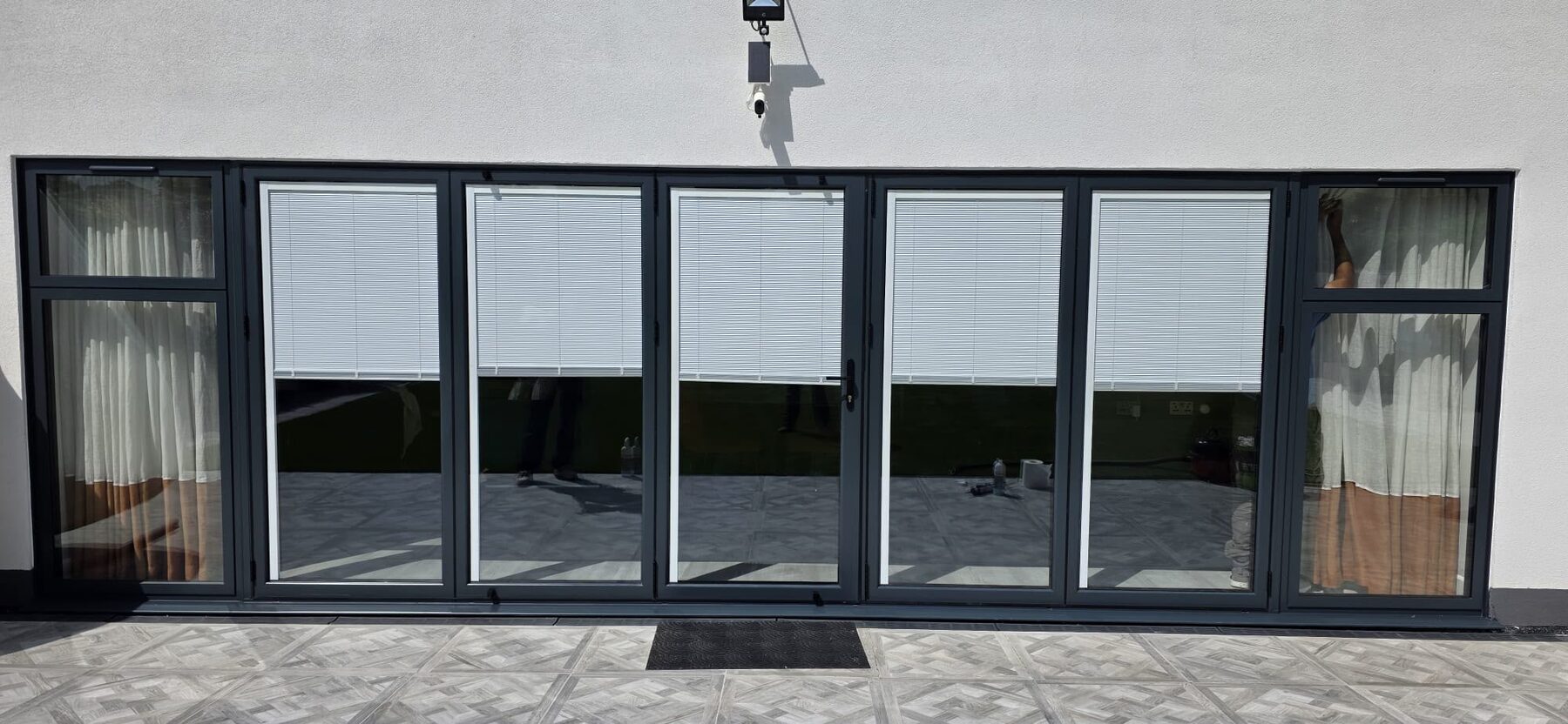 Anthracite aluminium bifolding doors with fixed side screens across a rendered rear elevation