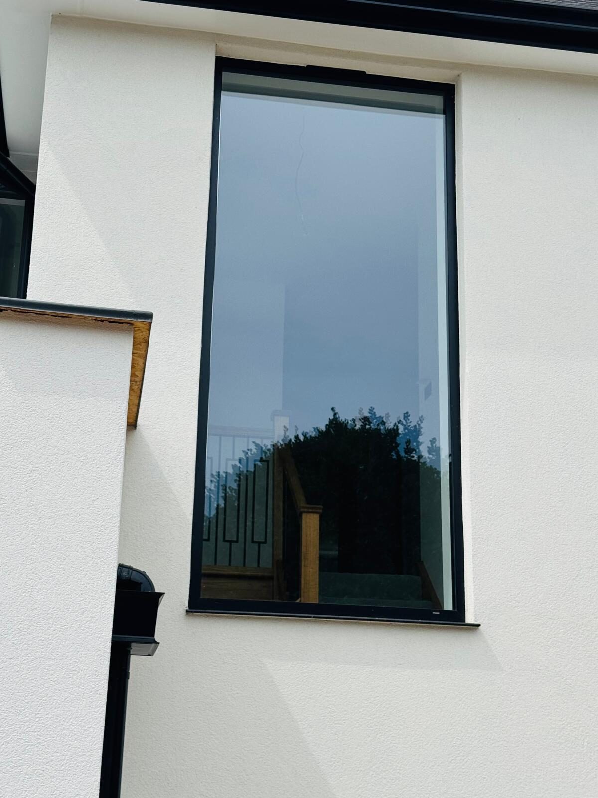 Tall slim-framed black picture window set into white render